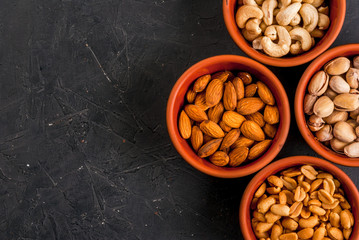 Four bowls with different nuts on a stone kitchen table: cashews, almonds, peanuts and pistachios, copy space