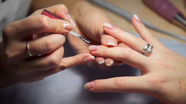 Master of manicure covers woman's nails by transparent nail polish, woman comes to the manicure salon, nail care, business in beauty