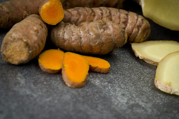 turmeric slices and ginger root sliced on gray background