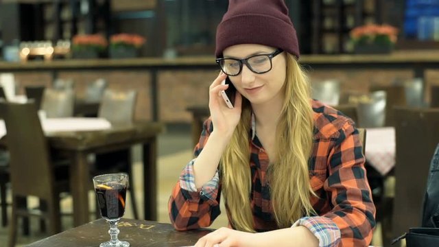 Hipster girl sitting in the cafe and talking on cellphone, steadycam shot
