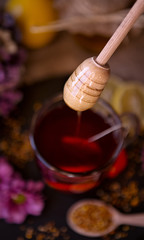 dripping sweet honey from wooden dipper on cup of tea close-up.