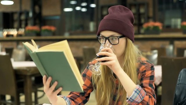 Hipster girl reading book and drinking beverage in the cafe, steadycam shot
