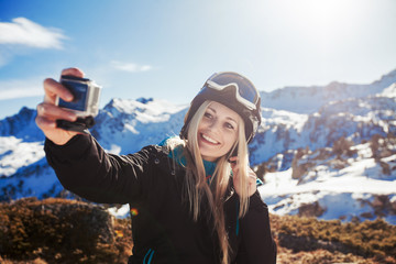 woman in the mountains winter holidays dress in a ski suite take photo on the action camera