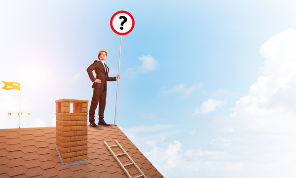 Businessman on brick house roof showing banner with question mark. Mixed media