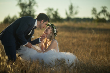 Young wedding couple enjoying romantic moments outside on a summer meadow. Happy groom and bride walking on summer sunset meadow