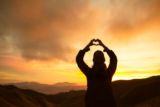 Love it in the air. Woman holding up heart against a beautiful sunset.