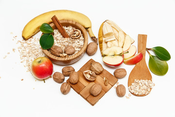 There are Banana,Apple,Walnuts in the Wooden Plate and Rolled Oats,Wooden Spoon,Trivet,with Green Leaves,Healthy Fresh Organic Food on the White Background,Top View