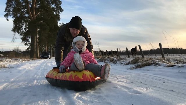 Dad pushes her daughter on a rubber inflatable snow tube in slow motion