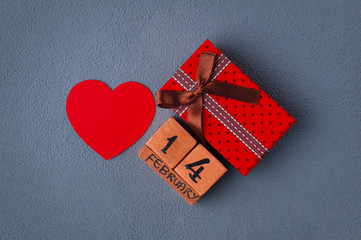 Red paper heart with wooden calendar show of February 14 and gift box on a grey background