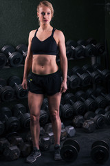 Fototapeta na wymiar Young woman standing by a stack of free weights at a gym