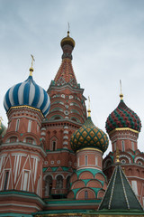 Fototapeta na wymiar St. Basil's Cathedral exterior showing decorative red brick facade and colorful onion domes topped with Orthodox crosses against a blue sky with thin clouds. 