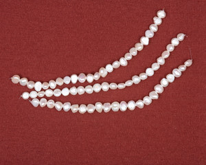 Three strings of natural white freshwater pearl beads on red fabric background