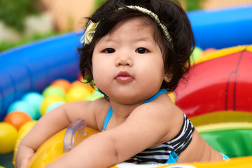 Fototapeta na wymiar Asian baby girl in swimsuit and float swimming in pool with balls