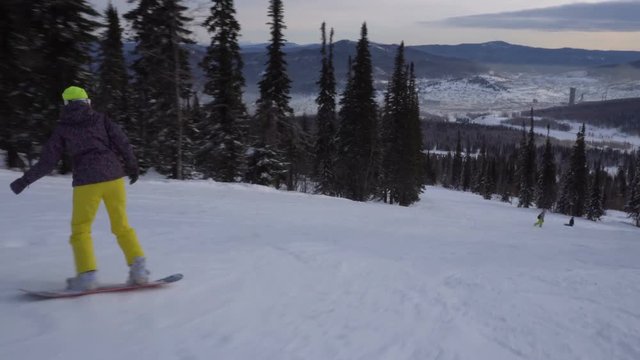 Woman snowboarder is drifting fast on snow-covered slope at mountains peak