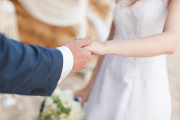 Obraz na płótnie Canvas Groom holding bride's hand at ceremony closeup