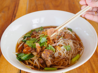 beef noodle with hot soup in a brown bowl with a Pair of Chopsticks put on wooden table. Asia food