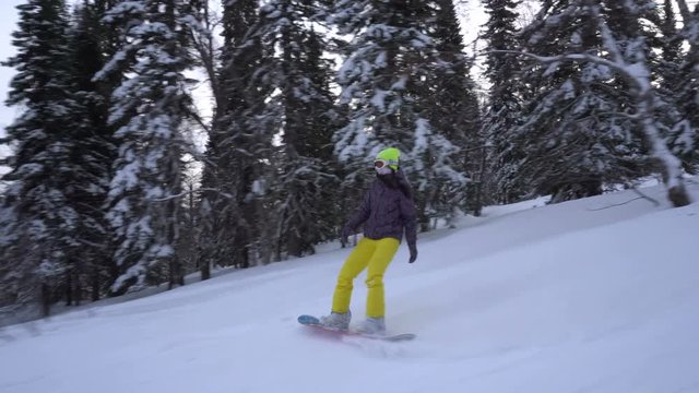 Woman is riding down fast on a snowboard from snow-covered mountains slope at cloudy day