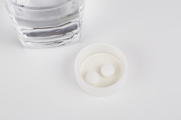 Round white pills and glass of water on a table.