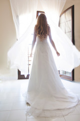 Bride in white dress standing in front of an open window