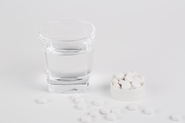 Round white pills and glass of water on a table.