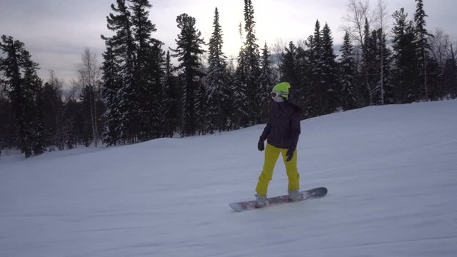 Woman is drifting fast on a snowboard from mountains slope at cloudy winter day