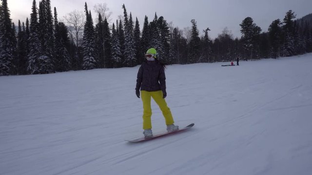 Front view woman is drifting fast on a snowboard from mountains slope at cloudy winter day