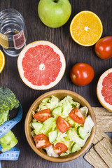 Food for diet and measuring tape on a dark wooden table.
