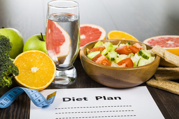 Food and sheet of paper with a diet plan on a dark wooden table.