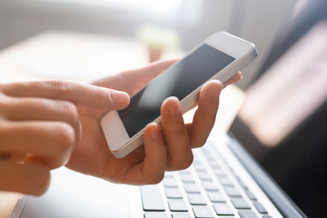 Finger pointing to phone screen, laptop in the bachground, informal business atmoshere