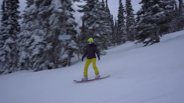 Young woman is drifting a snowboard fast on the snow-covered slope at winter cloudy day