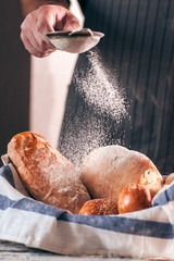 Sprinkling fresh bread with flour close-up. Baker decorating warm soft tack with sugar powder, free...