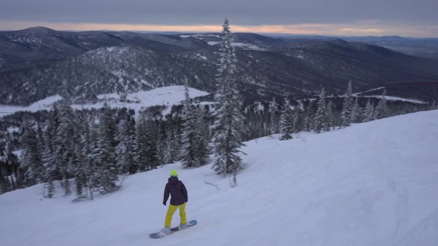 Woman is drifting a snowboard fast on the background of mountain's valley at winter cloudy day