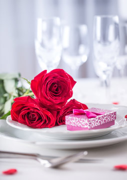 Table setting for valentines or wedding day with red roses. Romantic table setting for two with roses plates cups and cutlery.
