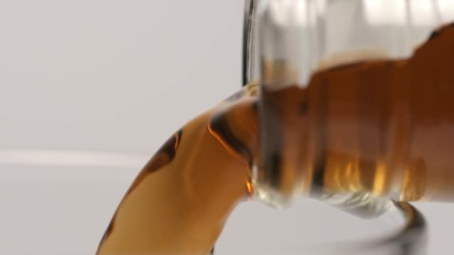 SLOW MOTION: Macro shot of pouring of a brown beverage from a glass bottle - side view