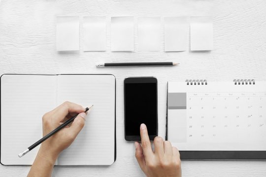 Hand  touch on a mobile phone black screen. , Hand-written in a notebook on a desk, top view.