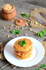 Pea patties on a white plate. Spicy vegan patties cooked from yellow dried peas and decorated with fresh parsley. Decorative barrel, fresh parsley on old wooden background. Vegan dish concept. Closeup