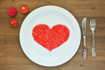 Red heart on a white plate. Love and romance. Valentine's Day. Romantic dinner by candlelight