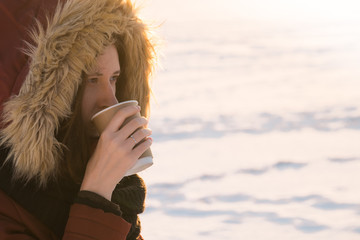 Having hot drink outdoors in winter. Young female person enjoying a cup of coffee to go at sunset of a cold winter sunny day