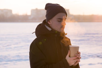 Hot steaming drink in male hands outside. Male person holding cup of coffee or tea at sunset of a sunny cold winter day