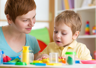 Obraz na płótnie Canvas Kid boy with teacher play clay at home, kindergarten, daycare center or playschool