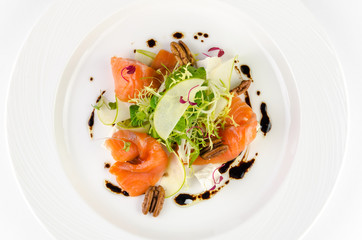 Marinated salmon with feta cheese, green apple, pecan and soy sauce on a plate on a white background, top view closeup