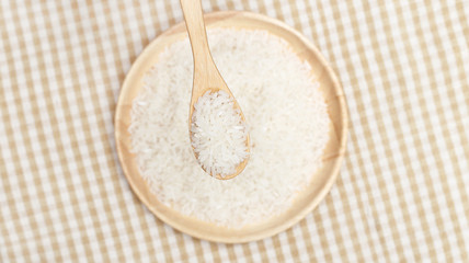 Spoon with Uncooked white rice on wooden plate 