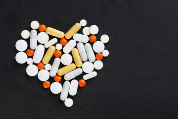 Many various pills and tablets as a heart lie on black background