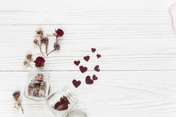 stylish hearts in glass jar and roses flat lay on white wooden b
