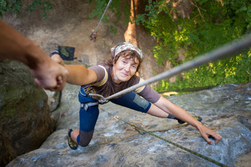 A male rockclimber is helping to old smiling female climber to reach a peak of mountain. Man giving...