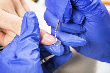 Manicure specialist care by finger nail in beauty salon.Gel nails.  Finger closeup isolated on blue...