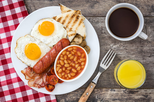 Traditional full English breakfast with fried eggs, sausages, beans, mushrooms, grilled tomatoes and bacon on wooden background.Top view
