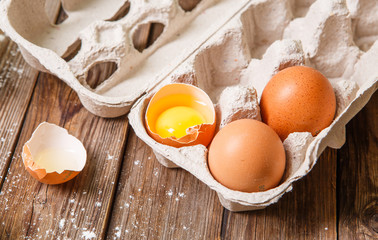 Fresh eggs, one of which was broken, on a wooden table.