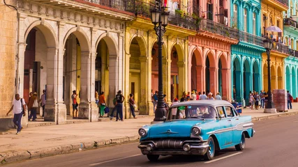  Een blauwe oldtimer taxi rijdt door Habana Vieja voor een kleurrijke gevel © Julian Peters Photos