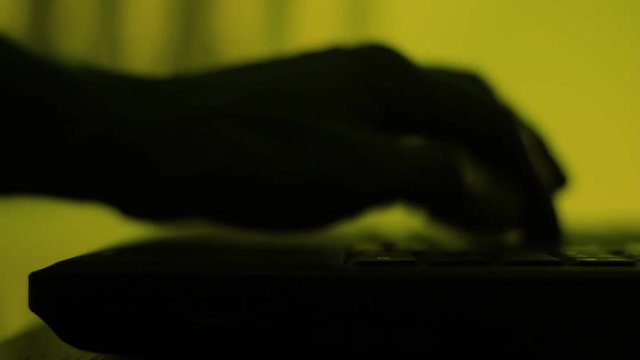 Shadow, silhouette of a male palm hand, typing on the laptop keyboard in the darkness.